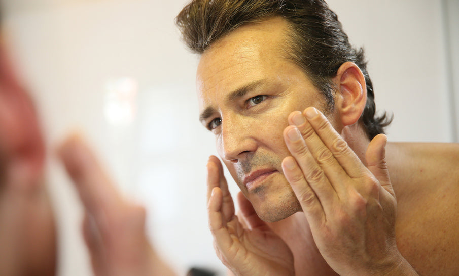 Man leaning toward a bathroom mirror, closely checking his face for redness and flaking