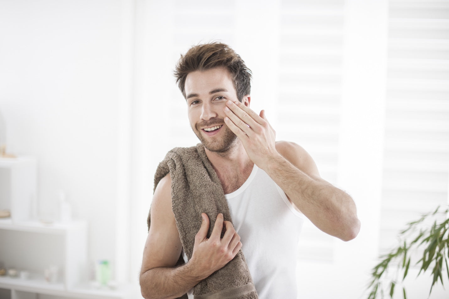 Man applying nighttime moisturizer to his face with a towel around his shoulders