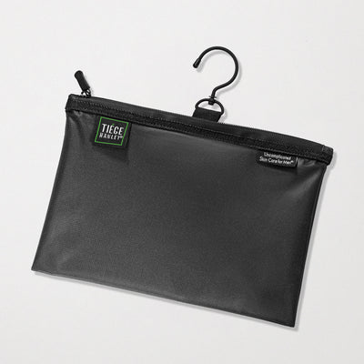 A black waterproof travel pouch with a hanging hook, featuring a zipper closure and branded with the Tiege Hanley logo.